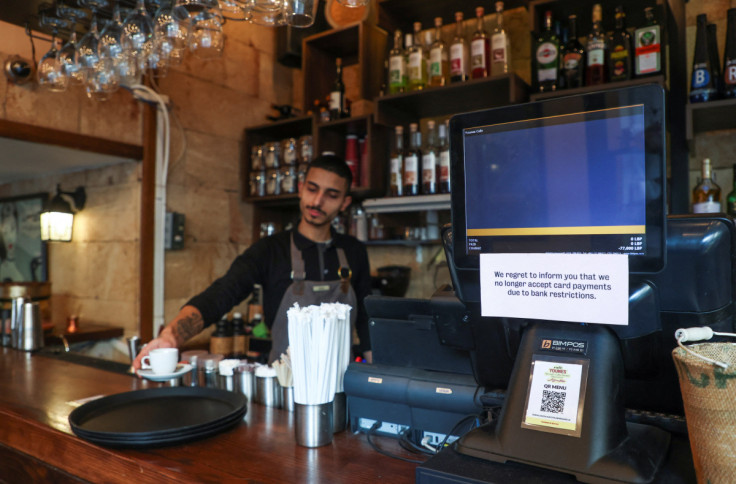 An employee serves coffee as a paper with a restriction is placed on a screen at a coffee shop in Beirut
