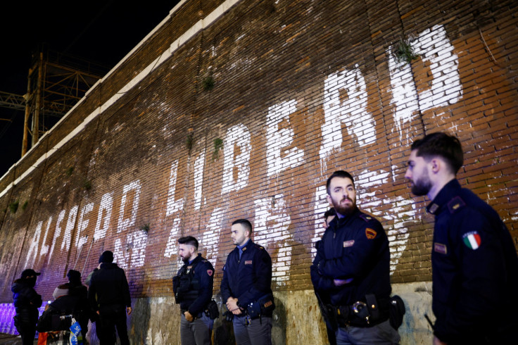 Police officers stand near a writing on a wall asking for freedom for Italian anarchist Alfredo Cospito