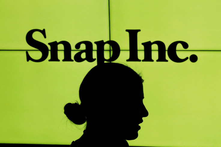 A woman stands in front of the logo of Snap Inc. on the floor of the New York Stock Exchange (NYSE) while waiting for Snap Inc. to post their IPO, in New York City