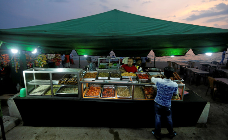 A vendor arranges food items at a food stall near a main road by the beach in Colombo