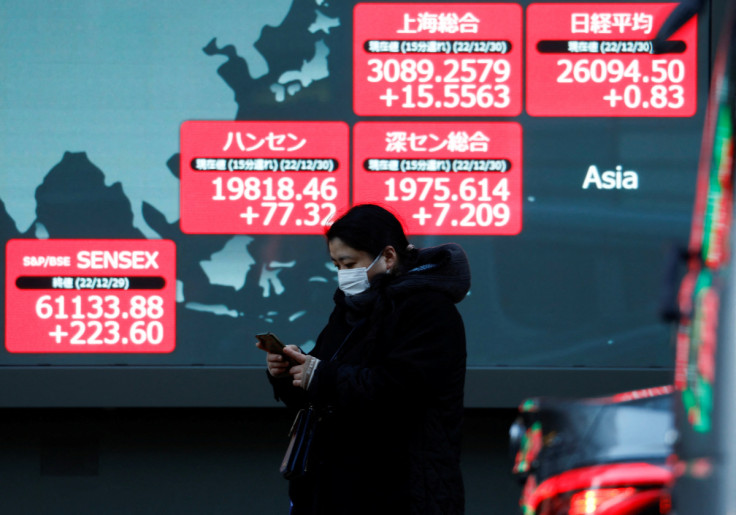 A passerby walks past an electric screen displaying various Asian countries' stock price indexes outside a brokerage in Tokyo