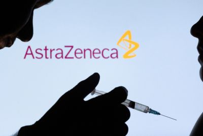 People pose with syringe with needle in front of displayed AstraZeneca logo