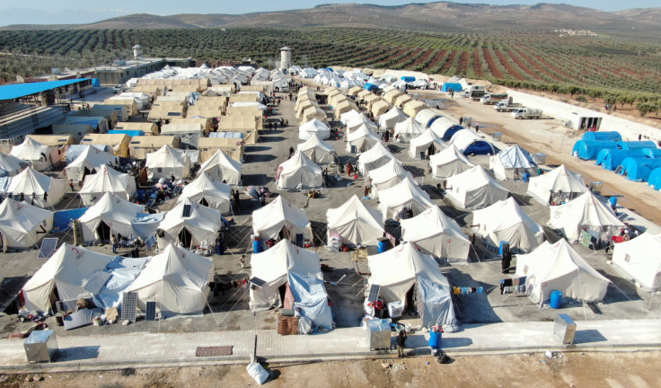 Displaced people walk outside tents at a camp for earthquake survivors, on the outskirts of rebel-held town of Jandaris
