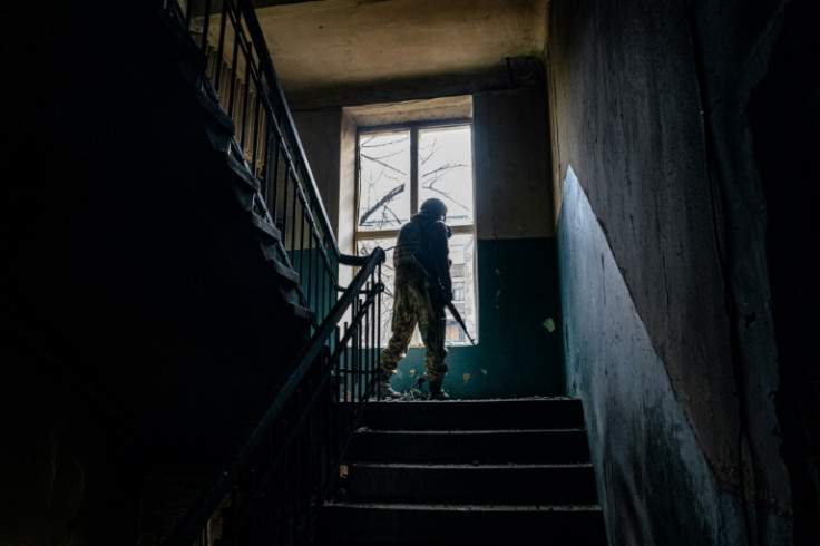 A Ukrainian soldier looks through a broken window of a damaged residential building in Bakhmut