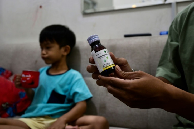 Riski Agri, right, displays a bottle of cough syrup that was consumed by his son Farrazka which caused him kidney problems