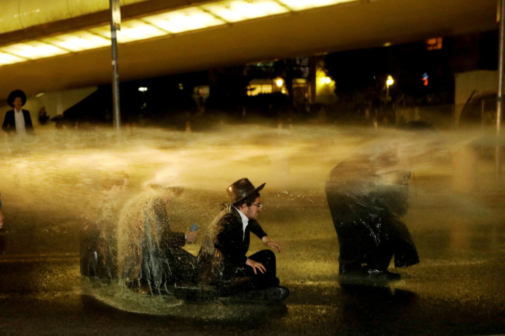 Israeli ultra-Orthodox Jewish men sit as a water canon is activated during a protest