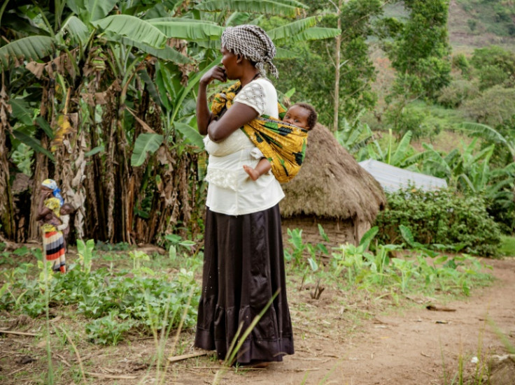 A woman carries a child while standing at her plot the day after the attack