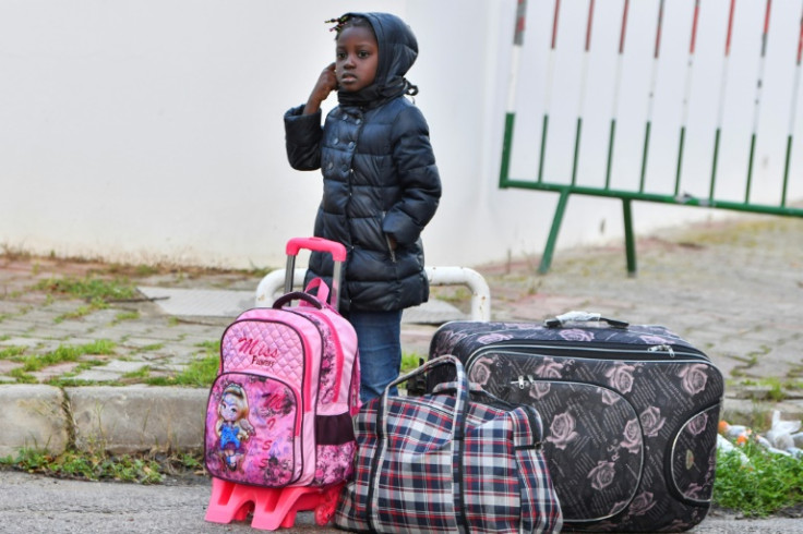 A girl in Tunisia waits by luggage as sub-Saharan African migrants board a bus taking them to a repatriation flight leaving Tunis for their countries of origin on March 4