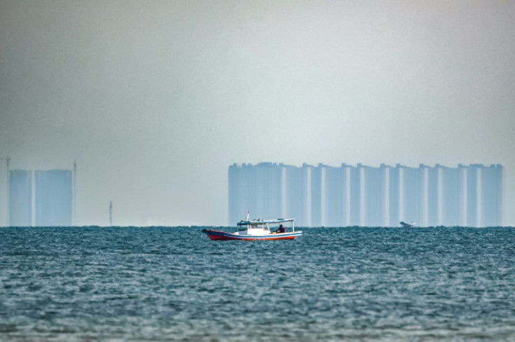 A man fishes off Pari, as buildings located in the northern part of nearby Jakarta are seen in the distance