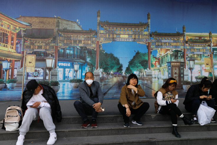 People rest in front of a board with an image of the tourism site of Qianmen street, in Beijing