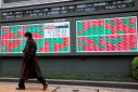 Man walks past an electronic board showing Japan's Nikkei average and stock prices outside a brokerage, in Tokyo