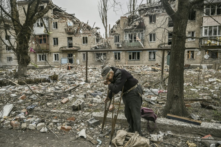 An old man on crutches gathers wood in the ruins of Avdiivka