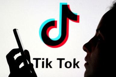 A person holds a smartphone as Tik Tok logo is displayed behind in this picture illustration