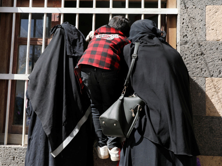 Women and a boy wait for a foodstuff assistance vouchers at an aid distribution center in Sanaa