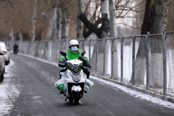 A Meituan delivery worker rides a scooter carrying vegetables on a snowy day in Beijing