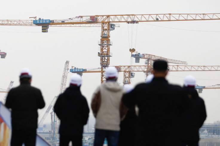 People look on near cranes standing at a construction site in Beijing