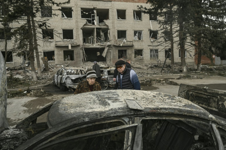 An eldery couple looks at a burned car in front of a destroyed building in the city of Sloviansk on March 27, 2023