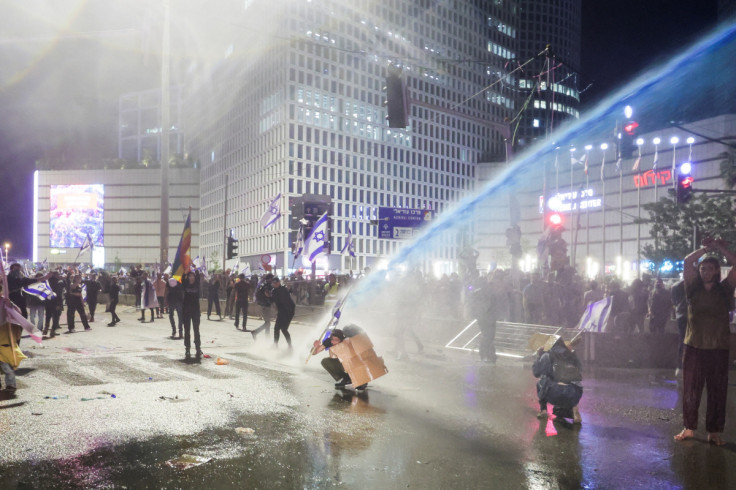 Israeli protesters react as a water cannon is used to disperse the people attending a demonstration against Israeli Prime Minister Benjamin Netanyahu and his nationalist coalition government's plan for judicial overhaul, in Tel Aviv