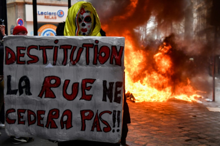 A protester holds a placard which reads "Impeachment: the streets will not back down" in front of a pile of burning garbage bins during a demonstration in Paris on Tuesday