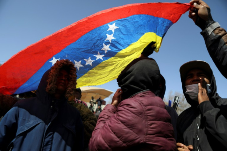 Migrants holding a Venezuelan flag protest outside an immigration detention center in northern Mexico where dozens perished in a blaze