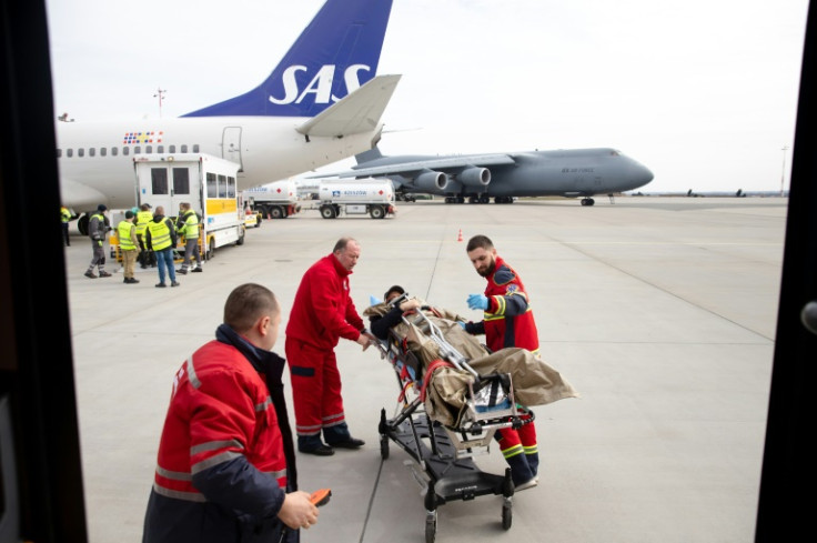 Ukrainian medical personnel bring a wounded soldier to the Norwegian plane as a military transport aircraft taxis nearby