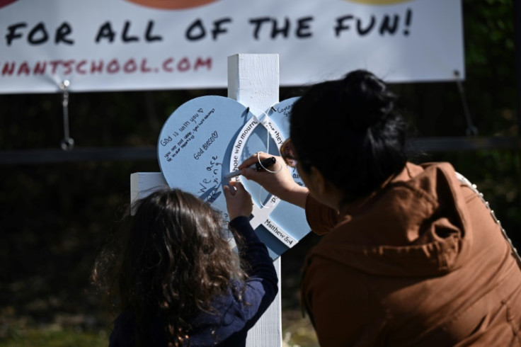 A mother helps her daughter write a message on a cross erected for one of the young victims of a shooting at The Covenant School in Nashville, Tennesse