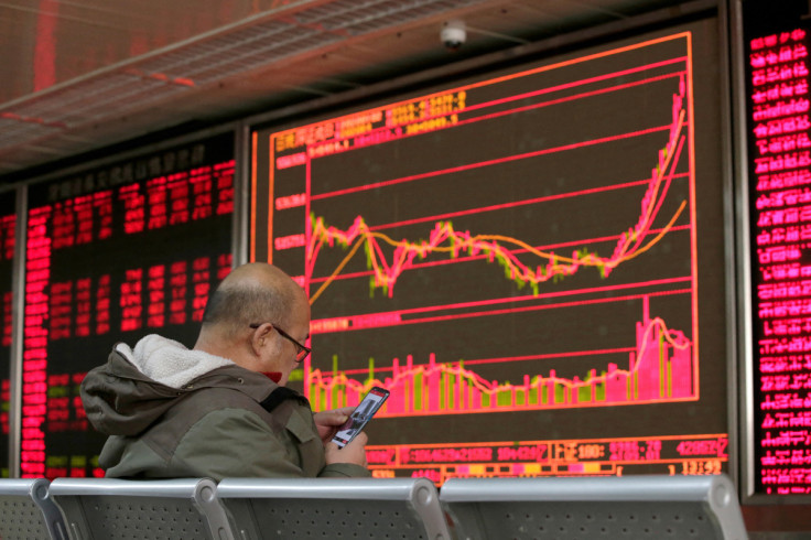An investor looks at his mobile phone in front of a board showing stock information at a brokerage office in Beijing, China