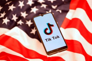 TikTok logo is displayed on the smartphone while standing on the U.S. flag in this illustration
