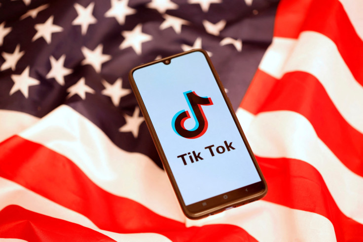 TikTok logo is displayed on the smartphone while standing on the U.S. flag in this illustration