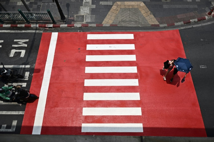 Pedestrians shelter from the sun using an umbrella at a crosswalk in Bangkok