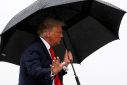 U.S. President Donald Trump walks without a mask and carries an umbrella while boarding Air Force One as he departs Washington
