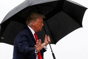 U.S. President Donald Trump walks without a mask and carries an umbrella while boarding Air Force One as he departs Washington