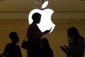 women uses her iPhone mobile device as she passes a lighted Apple logo at the Apple store in New York