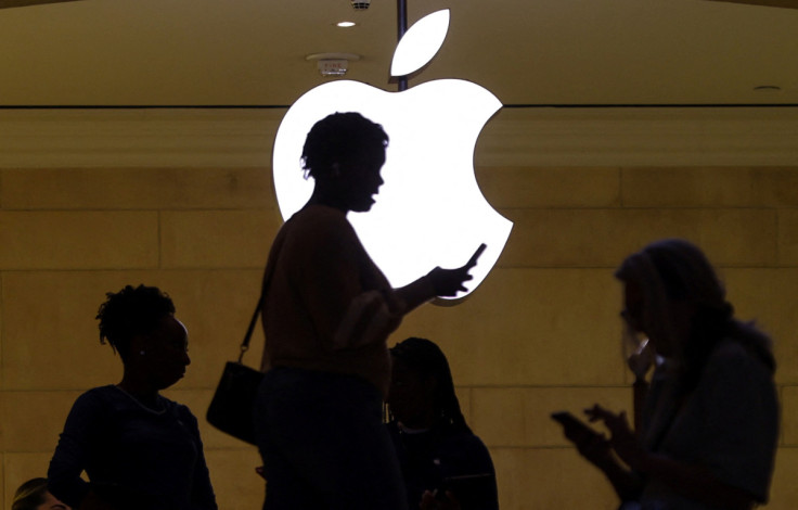 women uses her iPhone mobile device as she passes a lighted Apple logo at the Apple store in New York