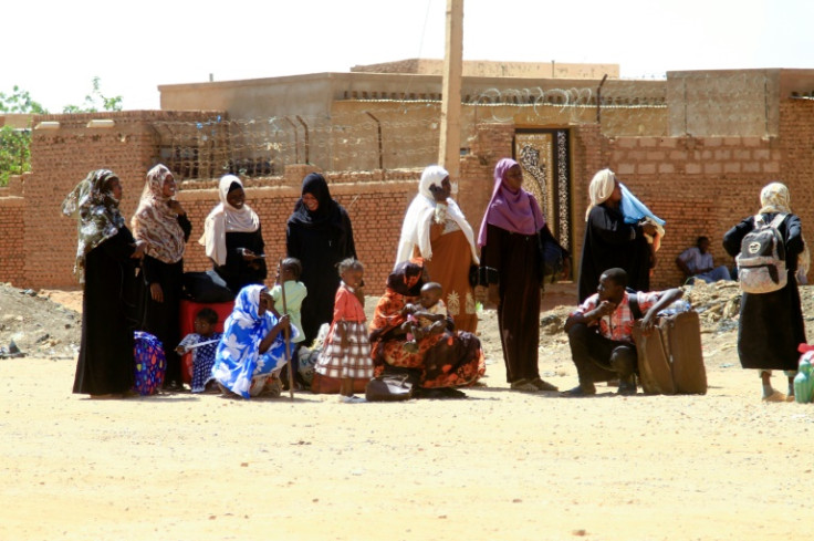 People fleeing street battles wait with their belongings along a road in the southern part of Khartoum