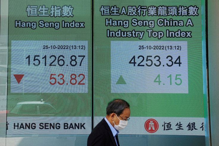 A person walks past a screen displaying the Hang Seng stock index at Central district, in Hong Kong