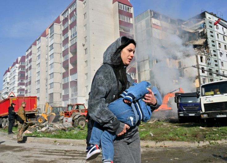A woman walks past damaged residential buildings as she carries a child in Kyiv