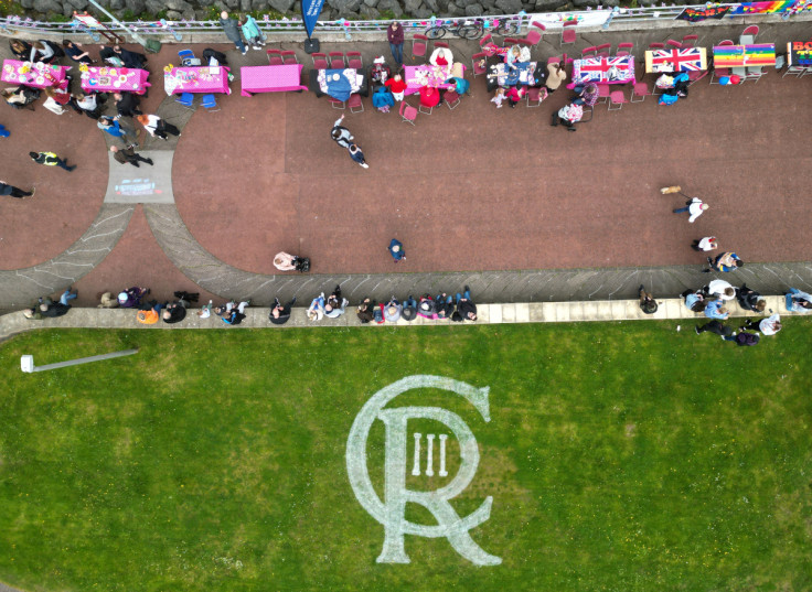 A logo for King Charles is seen on the grass next to people celebrating the Big Lunch on the prom
