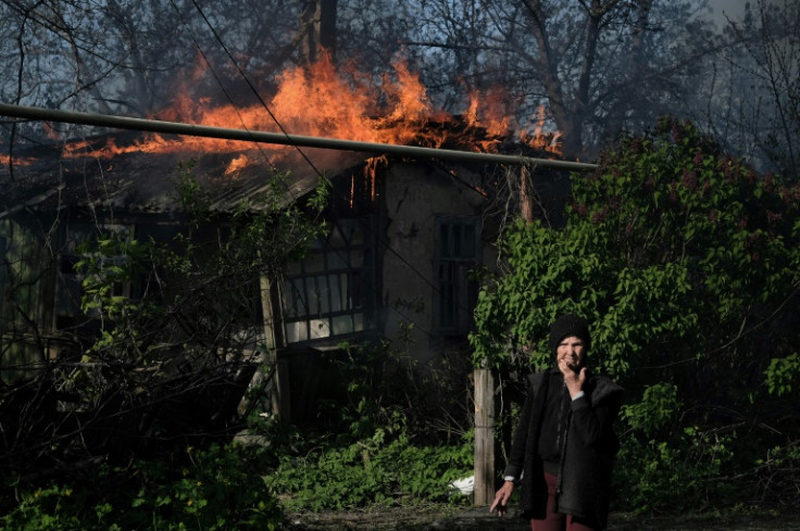 An elderly woman stands outside a burning house after shelling in the town of Chasiv Yar in east Ukraine