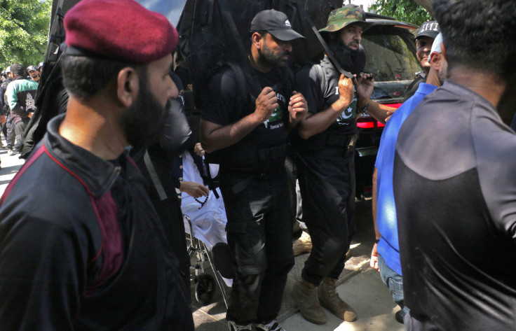 Pakistan's former Prime Minister Imran Khan sits in a wheelchair as his private security guards use shields to guard him upon his arrival to appear at a court in Islamabad