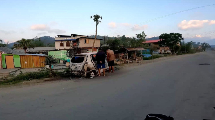 People stand near a burnt vehicle, in Manipur