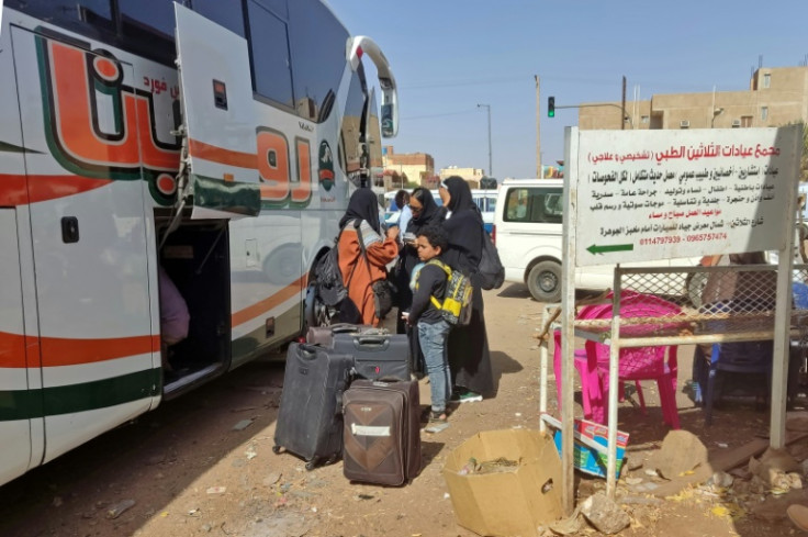 People wait with their luggage at a bus stop in southern Khartoum, preparing to join the exodus