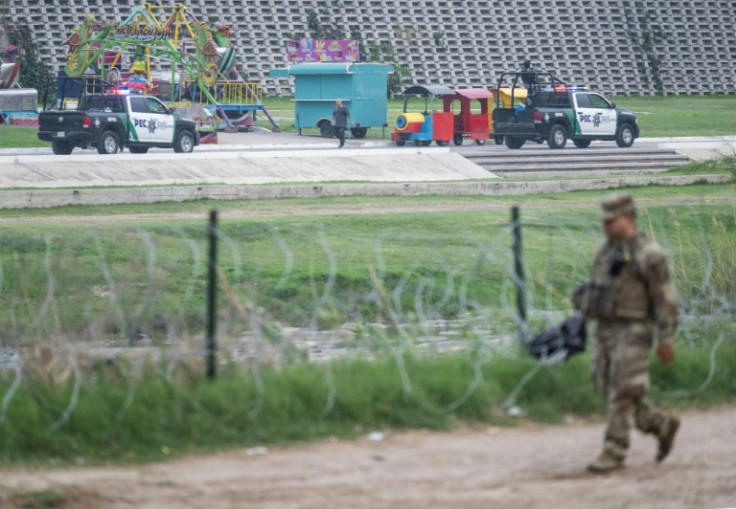 Mexican police patrol their side of the border as a member of the US military walks past a barb wire fence in Eagle Pass, Texas