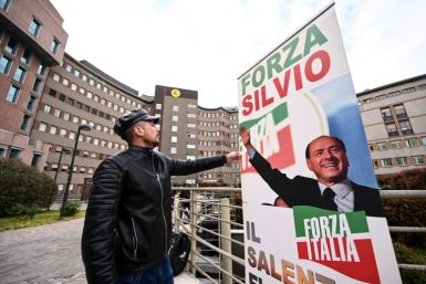 A man sets up a banner reading "Go Silvio!" in front of San Raffaele hospital