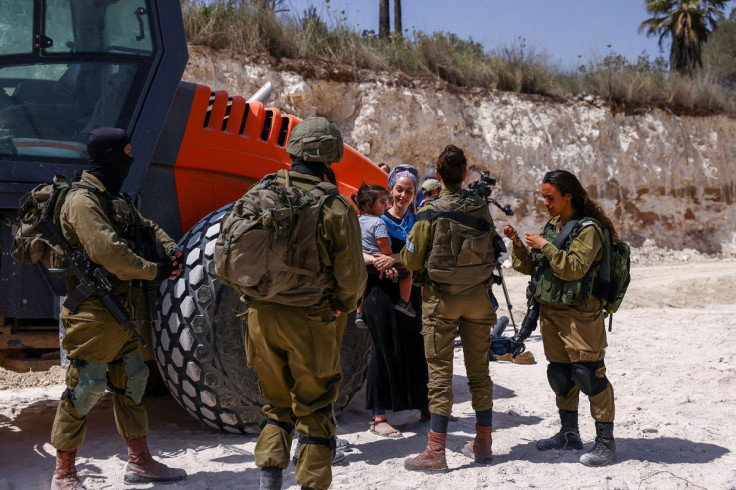 An Israeli settler carries a child in front of a group of Israeli soldiers in an area after structures were erected for a new Jewish seminary school, in the settler outpost of Homesh in the Israeli-occupied West Bank