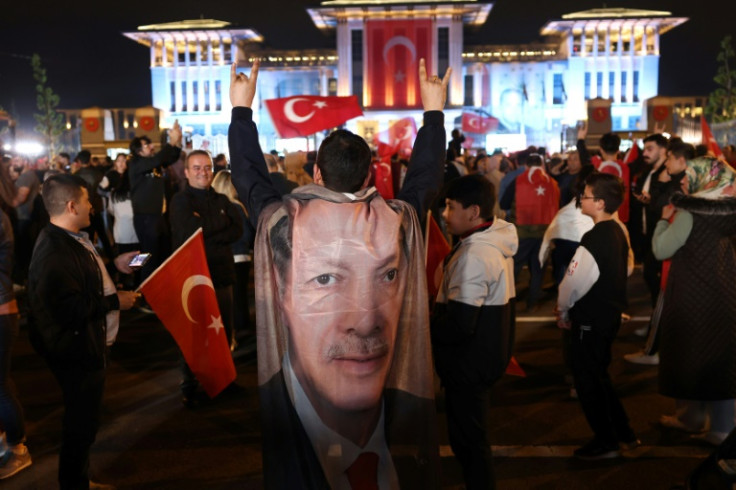 A supporter of the Turkish President Recep Tayyip Erdogan wears a flag with his image as people celebrate following his victory in the second round of the presidential election outside the  Presidential Palace in Ankara on May 29, 2023