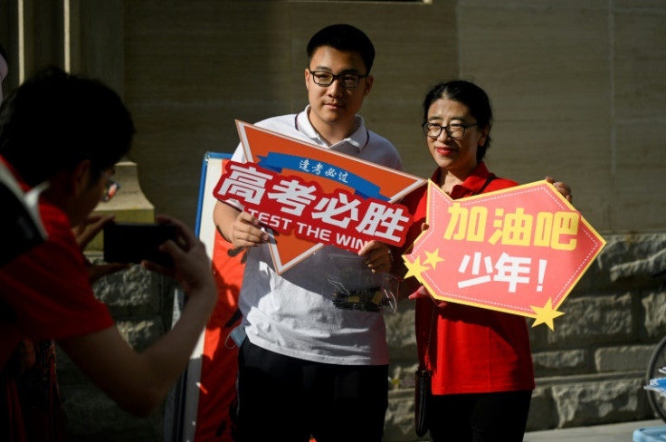 A student holding a poster reading 'Gao Kao, must win' poses for a picture with a volunteer before he enters a school on the first day of China's national college entrance examination, known as the gaokao, in Beijing on June 7, 2023.
