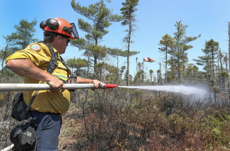 A firefighter sprays the ground as a water bomber flies by to dump a load of water on the fire, in Barrington Lake, Canada