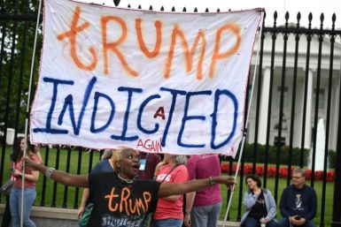 A woman marks the indictment of former US president Donald Trump by holding a banner in front of the White House in Washington