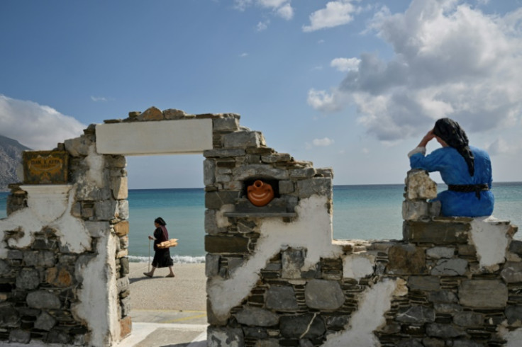 A woman carriying wood walks past a sculpure dedicated to Olympos' women in the village's port, Diafani